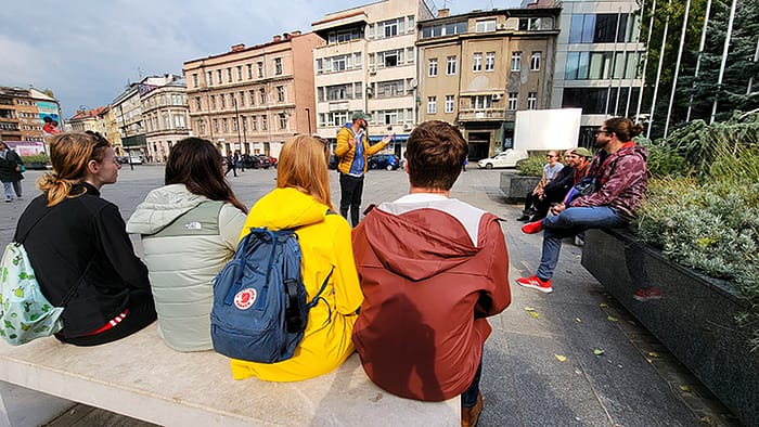 image of people sitting on benches listening to a tour guide
