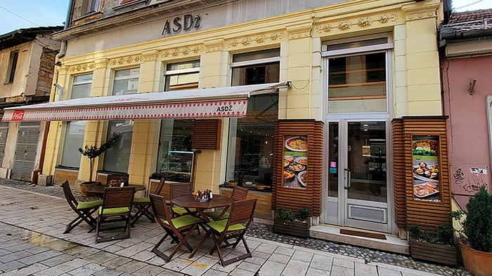 image of the outside of a yellow restaurant in Sarajevo with bistro tables