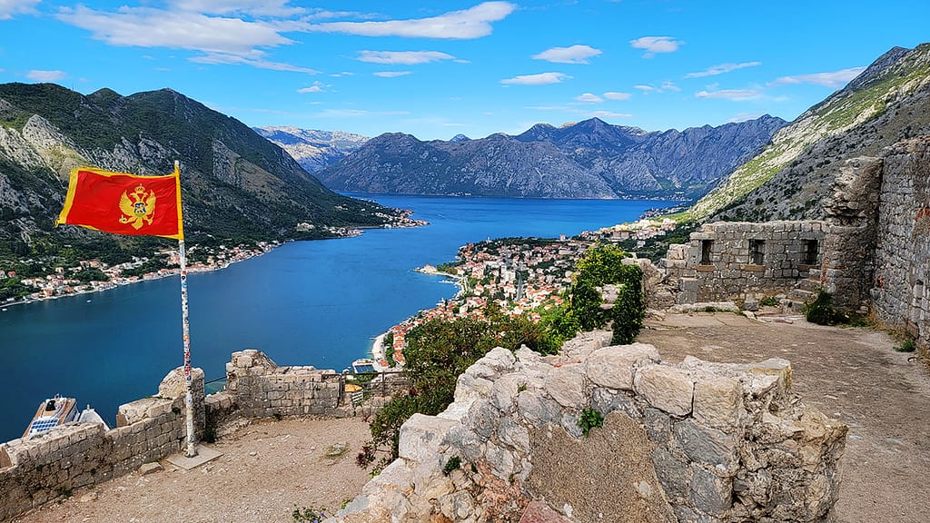 image of the flag of Montenegro with the Bay of Kotor in the background. This view is a great reason for why visit Montenegro.