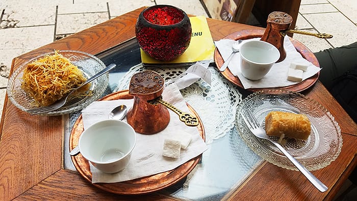 image of a small table with plates of baklava and copper settings containing traditional Bosnian coffee