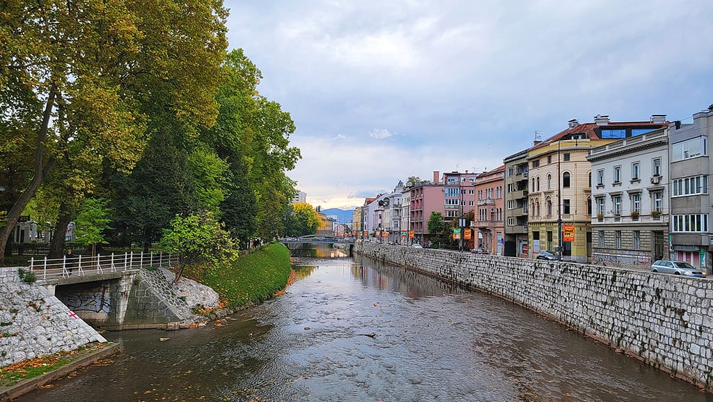 Image of the Miljacka River in Sarajevo with trees and buildings lining the streets on both sides.