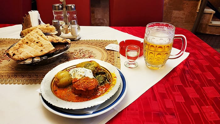 image of a table with a silver dish containing stuffed vegetables, a mug of beer, and small glass of local fruit brandy