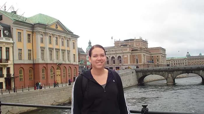 Picture of a woman in a black sweatshirt standing in front of yellow and orange buildings and a river in Stockholm, Sweden.